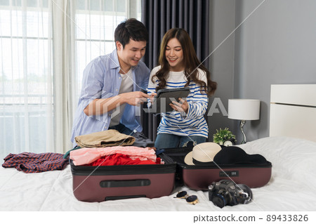 couple writing tablet and packing clothes into suitcase on bed at home, planning travel holiday. couple writing tablet and packing clothes into suitcase on bed at home, planning travel holiday. 89433826