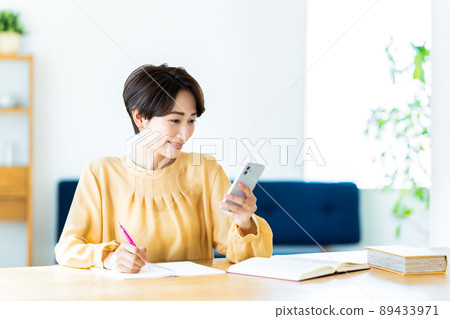 Middle-aged woman using a smartphone while studying at home Middle-aged woman using a smartphone while studying at home 89433971