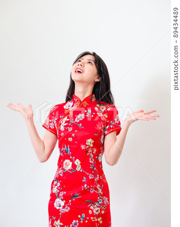 Portrait of young asian woman wearing traditional cheongsam qipao dress over isolated white background holding copyspace with two hands. 89434489