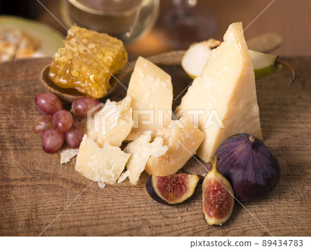 Cheese plate served with grapes, melon, figs, crackers, nuts and white wine on a wooden table Cheese plate served with grapes, melon, figs, crackers, nuts and white wine on a wooden table 89434783