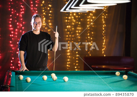 Billiard club. A young man in glasses standing by the table 89435870