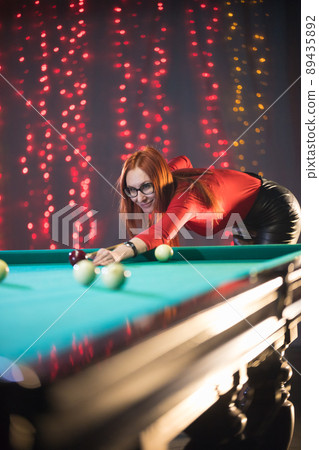 Smiling concentrated ginger woman playing billiard in nice architected club Smiling concentrated ginger woman playing billiard in nice architected club 89435892