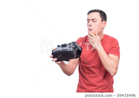 Puzzled man looking at VR goggles in studio Puzzled man looking at VR goggles in studio 89438496