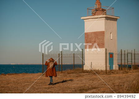 A woman walking along the coast near the sea. An elegant lady in a brown coat and a hat with fashionable makeup walks on the seashore 89439492