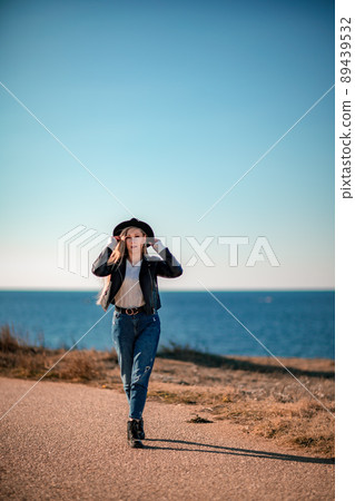 A blonde in a stylish black leather jacket walks along the seashore. A blonde in a stylish black leather jacket walks along the seashore. 89439532