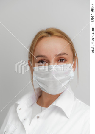 Close-up portrait of a young blonde woman in a medical mask on a light background. Virus protection. Coronovirus covid-19 The concept of a pandemic epidemic. Quarantine. Stay at home. Close-up portrait of a young blonde woman in a medical mask on a light background. Virus protection. Coronovirus covid-19 The concept of a pandemic epidemic. Quarantine. Stay at home. 89440990