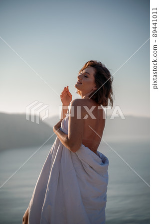 Woman wake up in bed wuth duvet and pillow over nature sea background outdoors. Back view. Good morning. Freedom concept. 89441011