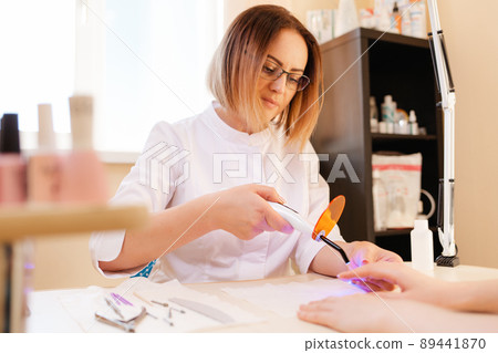 Medicine, nail Polish and prosthetic nail. A manicure master performs a procedure for prosthetics of the nail using an ultraviolet lamp 89441870