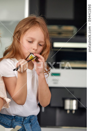 Cute smiling little girl with sushi on white background. Child girl eating sushi and rolls - commercial concept. Cute smiling little girl with sushi on white background. Child girl eating sushi and rolls - commercial concept. 89441898