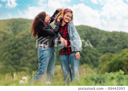 Mother happily decorates her teen daughter's hair with dandelions. In the background, the forest and the sky. The concept of summer outdoor recreation 89442093