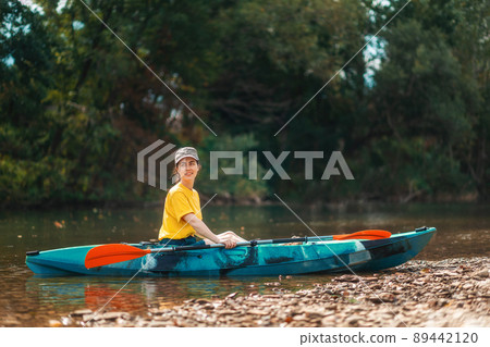 World Tourism Day. A young happy woman is sitting in a kayak on the river bank. Copy space. The concept of kayaking and outdoor activities World Tourism Day. A young happy woman is sitting in a kayak on the river bank. Copy space. The concept of kayaking and outdoor activities 89442120