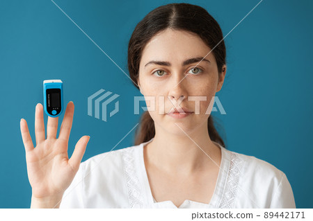 Portrait of woman doctor shows a pulse oximeter on her index finger. Blue background. The concept of check health and medical insurance Portrait of woman doctor shows a pulse oximeter on her index finger. Blue background. The concept of check health and medical insurance 89442171