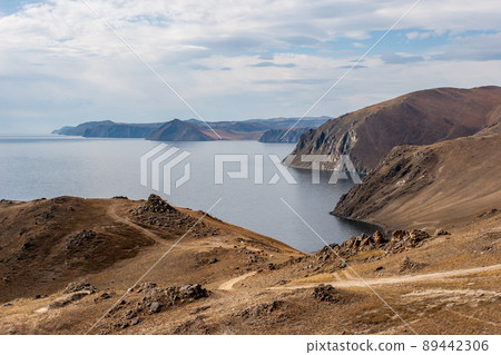High rocky shore of Lake Baikal. The road goes down to the lake. Clouds in the sky. Brown tones. Horizontal. High rocky shore of Lake Baikal. The road goes down to the lake. Clouds in the sky. Brown tones. Horizontal. 89442306