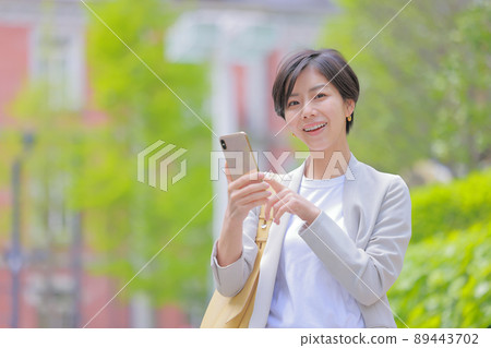 Early summer town_Woman operating a smartphone_Looking at the camera Early summer town_Woman operating a smartphone_Looking at the camera 89443702