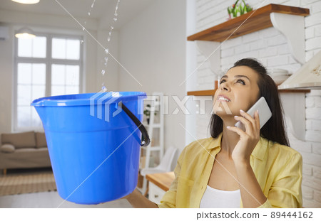 Woman with damaged roof and leaking ceiling in her house is calling repair service Woman with damaged roof and leaking ceiling in her house is calling repair service 89444162