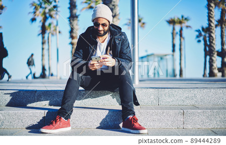 Millennial bearded man chatting via smartphone technology searching web app for installing Millennial bearded man chatting via smartphone technology searching web app for installing 89444289