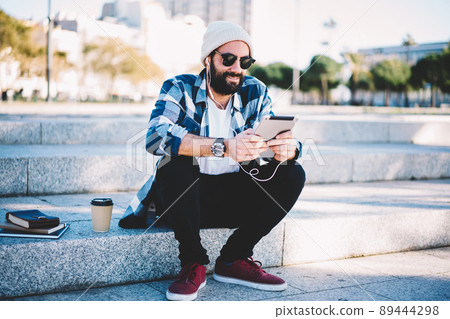 Turkish hipster guy in earphones and sunglasses watching video vlog via touch pad 89444298
