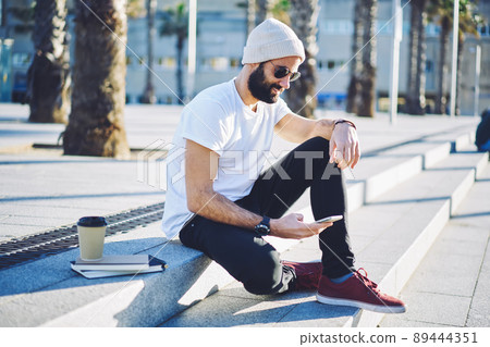 Handsome Middle Eastern user installing mobile app during social networking on leisure Handsome Middle Eastern user installing mobile app during social networking on leisure 89444351