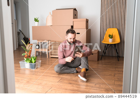 Mature man using his tablet while moving in new unfurnished apartment. 89444519