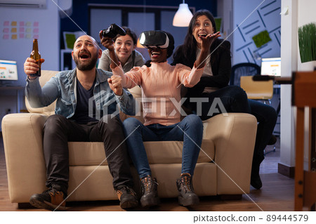 Diverse group of workmates playing video games with vr headset, enjoying virtual reality technology on game play with joystick. Cheerful people having fun at office party after work. Diverse group of workmates playing video games with vr headset, enjoying virtual reality technology on game play with joystick. Cheerful people having fun at office party after work. 89444579
