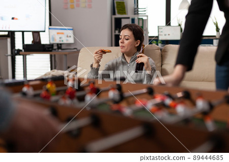 Portrait of cheerful woman eating pizza and drinking beer after work in business office with colleagues. Young person enjoying party celebration after hours, doing fun activity with friends. 89444685
