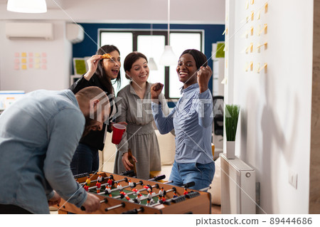 Happy woman celebrating foosball game win at office party after hours, enjoying alcoholic drinks with colleagues after work. Businesspeople having fun with leisure activity game. Happy woman celebrating foosball game win at office party after hours, enjoying alcoholic drinks with colleagues after work. Businesspeople having fun with leisure activity game. 89444686