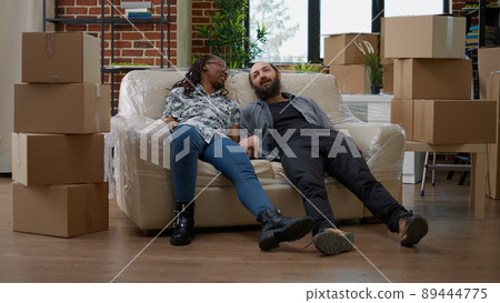 Multiethnic couple relaxing on sofa after unpacking furniture, preparing apartment space to move in together. Taking break on couch, decorating new rented home with belongings. Multiethnic couple relaxing on sofa after unpacking furniture, preparing apartment space to move in together. Taking break on couch, decorating new rented home with belongings. 89444775