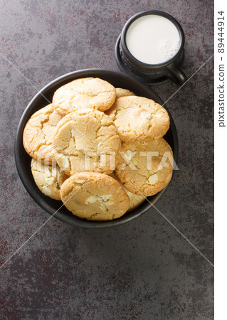 Fresh made Macadamia Cookies with white chocolate closeup in the black bowl and cup of milk close-up. Vertical top view 89444914