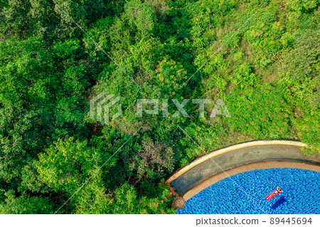 girl floating in the pool water relaxing on pink inflatable mattress in blue swimmingpool remote work and freelance top view green tree luxury eco hotel in Goa India 89445694