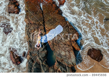 Young woman in a bikini and pareo with long train lying on the back on the sand near the waves of blue sea. Top view Young woman in a bikini and pareo with long train lying on the back on the sand near the waves of blue sea. Top view 89445698