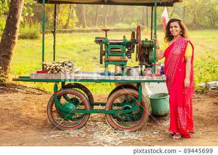 beautuful induan woman in red sari standing near sugarcane juice maker apparatus machine , plantation summer farm background. small business start up beautuful induan woman in red sari standing near sugarcane juice maker apparatus machine , plantation summer farm background. small business start up 89445699