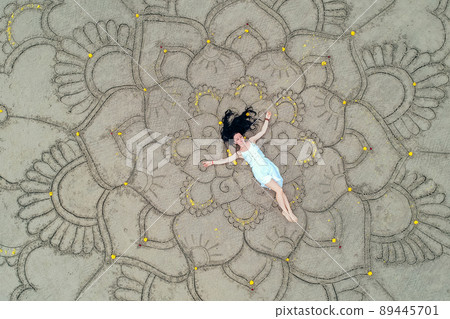 a large mandala painted on the sand on the ocean with a girl in the middle boho style. a large mandala painted on the sand on the ocean with a girl in the middle boho style. 89445701