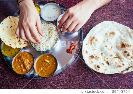 close up photo of Indian traditional vegetarian thali from rice, dal, potatoes, tomato salad on metal plate ,female hands roti india tortilla Chapati 89445704