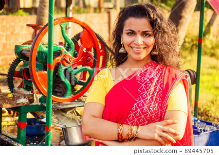 beautuful induan woman in red sari standing near sugarcane juice maker apparatus machine , plantation summer farm background. small business start up beautuful induan woman in red sari standing near sugarcane juice maker apparatus machine , plantation summer farm background. small business start up 89445705