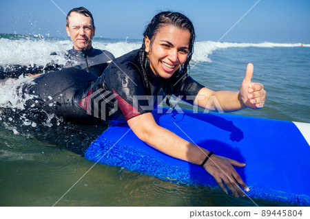 man instructor and indian woman showing thumbs up in surf class in Goa sea man instructor and indian woman showing thumbs up in surf class in Goa sea 89445804