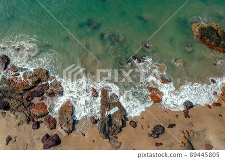 Young woman in a bikini and pareo with long train lying on the back on the sand near the waves of blue sea. Top view Young woman in a bikini and pareo with long train lying on the back on the sand near the waves of blue sea. Top view 89445805