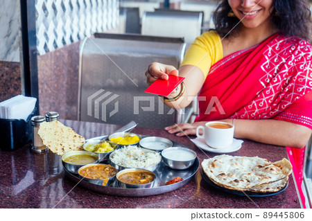beautiful brunette woman in red sari paying by plastic card for traditional thali with rise,curd,dal and masala tea beautiful brunette woman in red sari paying by plastic card for traditional thali with rise,curd,dal and masala tea 89445806