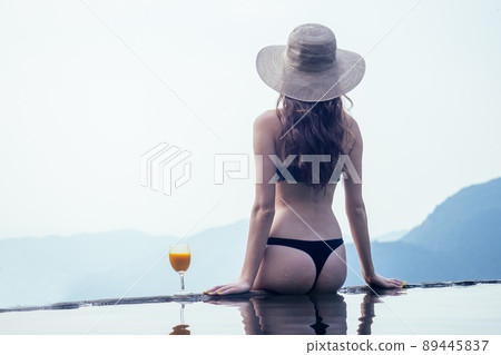 girl relaxing on inflatable pink donut in the infinity swimming pool at Goa india resort with coctail glass 89445837