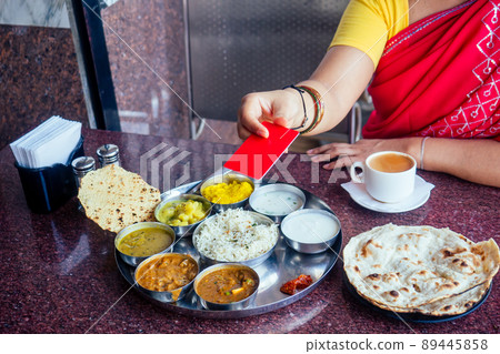 beautiful brunette woman in red sari paying by plastic card for traditional thali with rise,curd,dal and masala tea beautiful brunette woman in red sari paying by plastic card for traditional thali with rise,curd,dal and masala tea 89445858