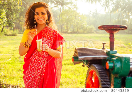 beautuful induan woman in red sari standing near sugarcane juice maker apparatus machine , plantation summer farm background. small business start up beautuful induan woman in red sari standing near sugarcane juice maker apparatus machine , plantation summer farm background. small business start up 89445859