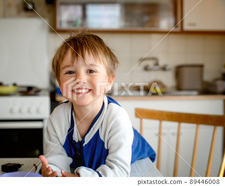 Happy smiling little kid having breakfast in the kitchen with cereal, milk and banana. Child boy likes to eat Happy smiling little kid having breakfast in the kitchen with cereal, milk and banana. Child boy likes to eat 89446008