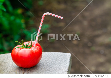 Ripe red tomato with straw on wooden surface. Fresh juice healthy food concept. Tomato as a vessel with fresh juice. Closeup, selective focus Ripe red tomato with straw on wooden surface. Fresh juice healthy food concept. Tomato as a vessel with fresh juice. Closeup, selective focus 89446485