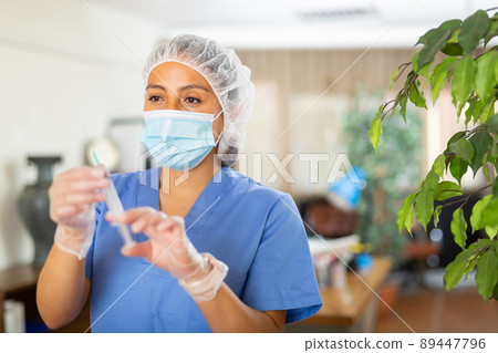 Female nurse wearing in face mask and medical uniform holding vial and syringe Female nurse wearing in face mask and medical uniform holding vial and syringe 89447796