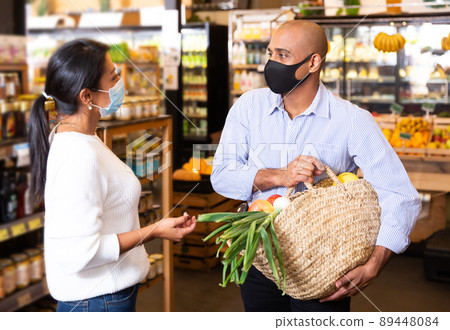 Smiling Latino in protective mask talking to woman in grocery store 89448084