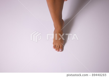 Womans leg stepping on a white floor. Female foot with a shadow. Womans leg stepping on a white floor. Female foot with a shadow. 89448283