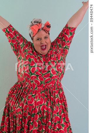 Plus size sexy model woman with trendy makeup, fashionable blonde in colorful dress posing at the cyan or light blue background in studio. 89448474