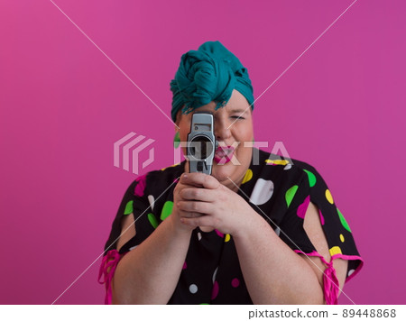 plus size smiling woman with funny emotional face expression with vintage camera in dress isolated on pink background, traveler on vacation, summer fashion style, excited tourist. 89448868