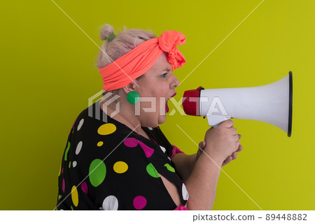 Funny plus size woman woman posing isolated on pastel green background studio portrait. People emotions lifestyle concept. Mock up copy space. Screaming in megaphone.  89448882