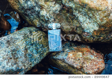 Transparent bottle of dark perfume with water drops lies on rocks. Top view. Concept of luxe perfumery and cosmetics Transparent bottle of dark perfume with water drops lies on rocks. Top view. Concept of luxe perfumery and cosmetics 89449647