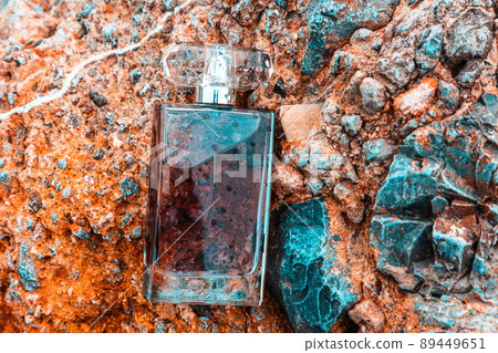 Close up of transparent bottle with dark perfume on rocks. Top view. Concept of luxe perfumery and cosmetics Close up of transparent bottle with dark perfume on rocks. Top view. Concept of luxe perfumery and cosmetics 89449651